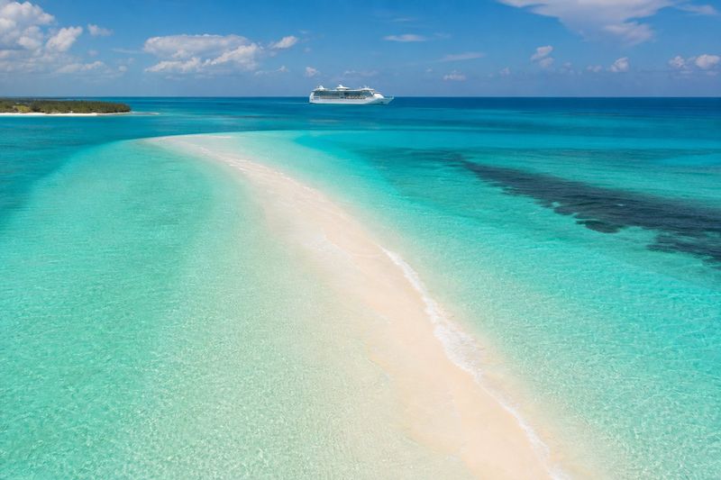 Aerial view of a turquoise Bahamas lagoon and white sandbar with a cruise ship on the horizon