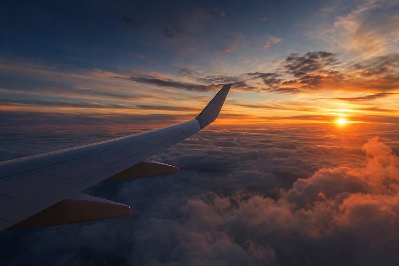 Aircraft wing above a golden sunset cloudscape at cruising altitude
